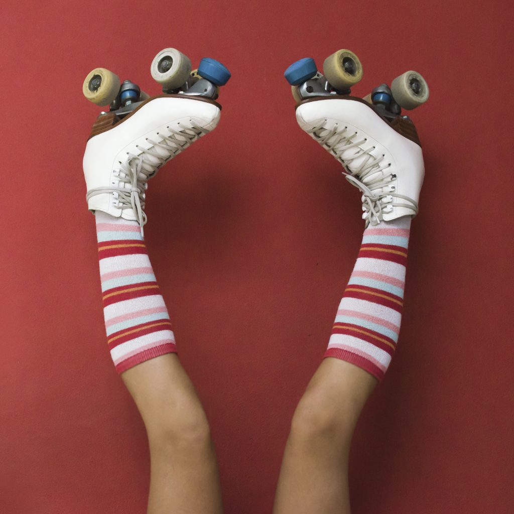 Girl's legs wearing long socks and rollerskates upside down against a wall